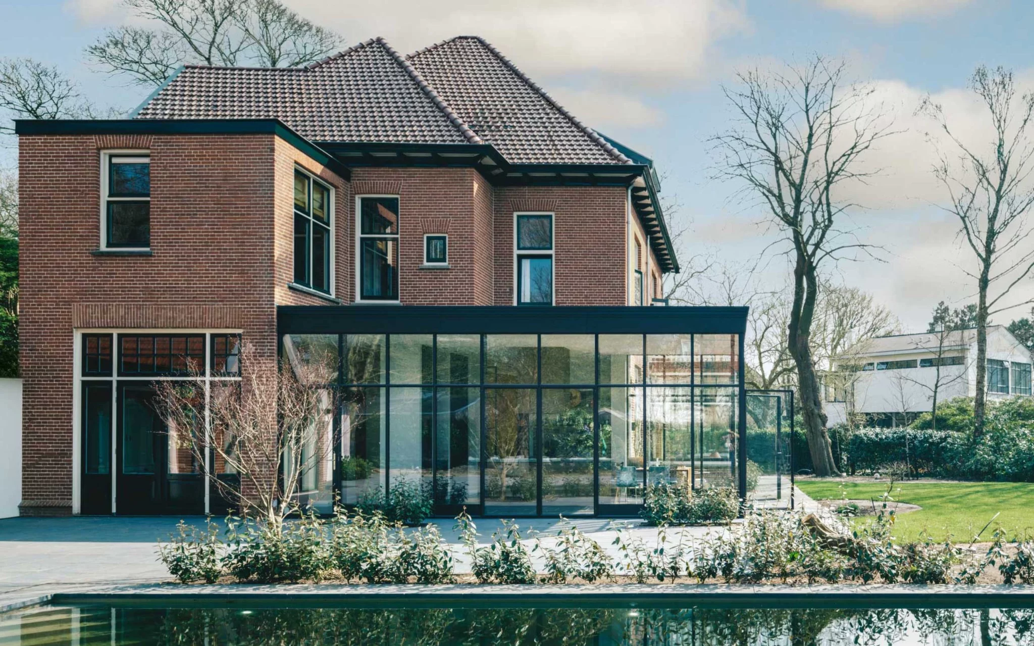Glazen uitbouw aan een bestaande woning, gezien vanuit de tuin