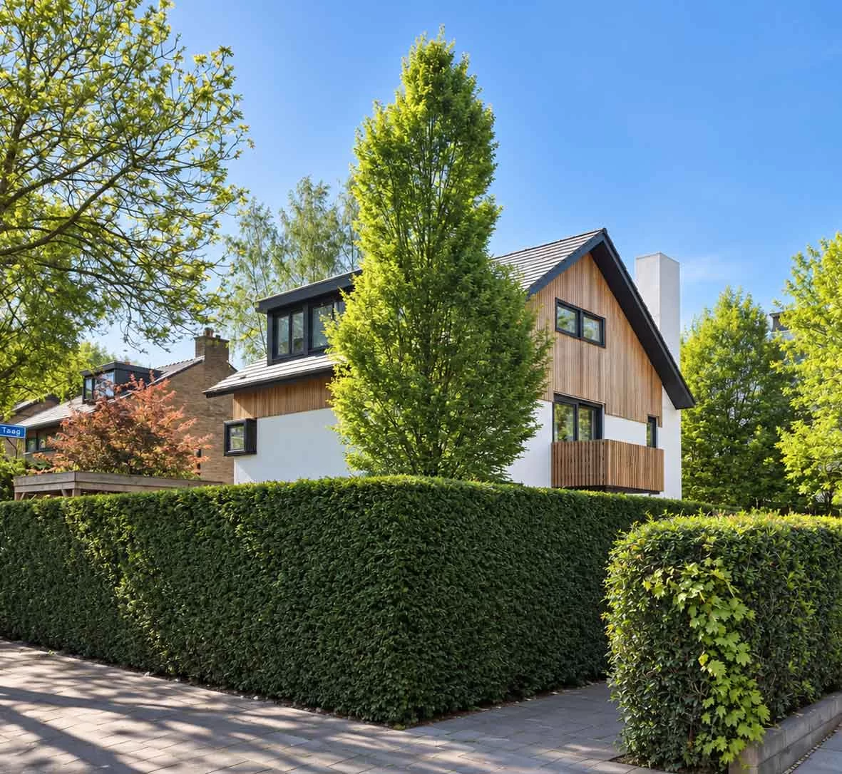 Straatbeeld van de woning met houten dakopbouw achter een groene haag