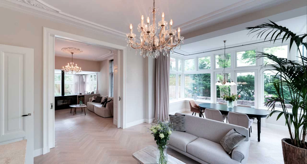 Woonkamer met ornamentenplafond en hoge ramen naar de tuin
